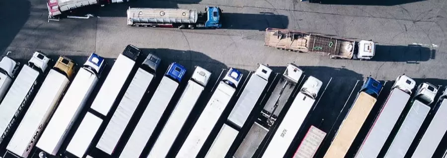 Parking dla ciężarówek widziany z góry — naczepy ustawione w rzędach, kilka pojazdów odstawionych bokiem